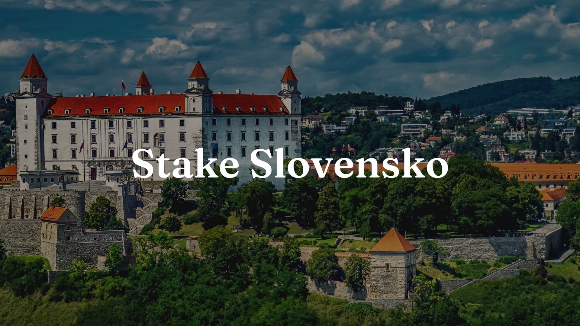 Stake Slovensko: Obrázok mesta na Slovensku s domami s červenými strechami a množstvom zelene. Na obrázku je tiež vidieť nápis Stake Slovakia.